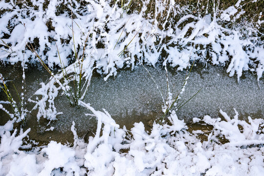 A frozen stream surrounded by snow-covered grass