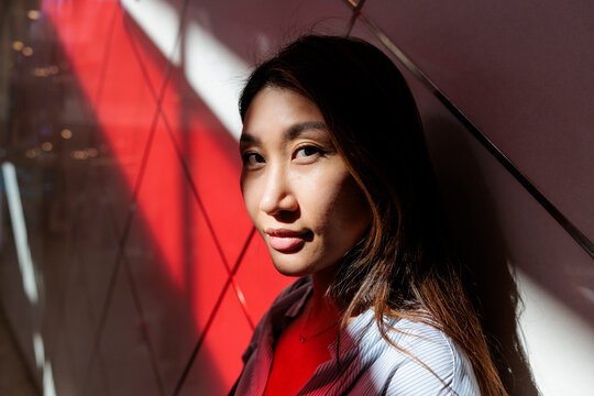 Woman in sunlight against red wall.