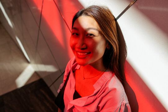 Smiling woman bathed in red light against a white wall.