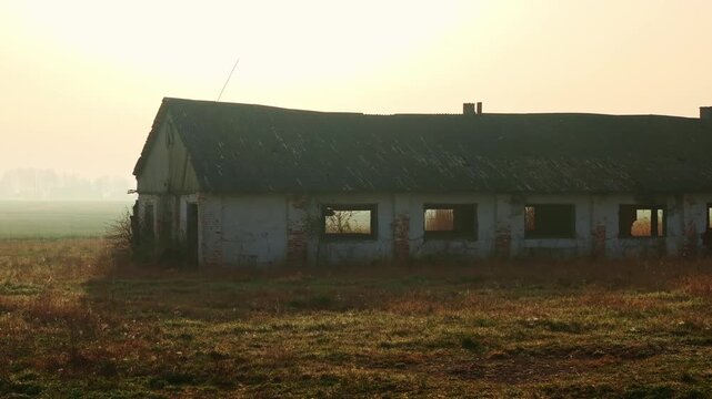Side moving drone passes abandoned soviet farm in misty sunset light spring