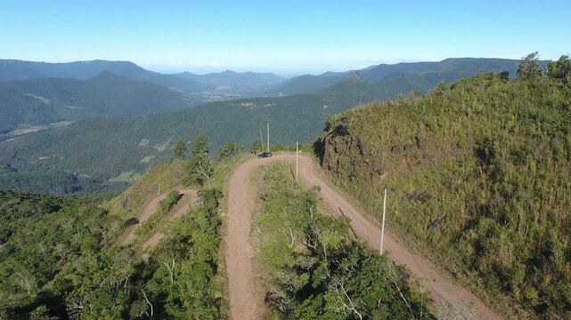 Cinematic drone aerial establishing shot revealing a winding s-curve dirt road at Serra do Rabisco mountains in Rio Grande do Sul Brazil. High quality 4K Apple ProRes 422 10-bit nature footage.