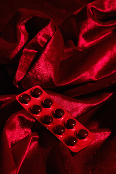 Red Fabric Surrounds a Blister Pack of Pills on Soft Surface