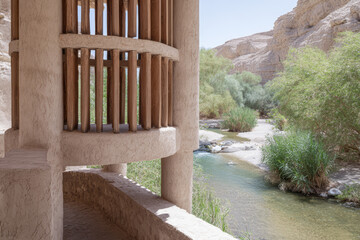 View of a structure near a river in a desert canyon with plants and mountains in the background during daytime
