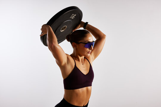 Strong woman lifting a weight plate above her head in a fitness 