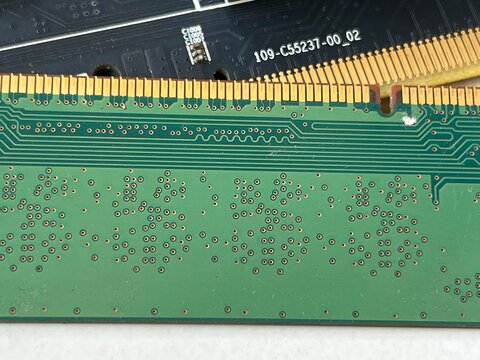 Close-up of a green RAM memory module showing gold-plated contacts, intricate circuit traces, and small surface-mount components on the PCB.