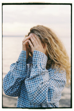 Woman standing near water covering her face