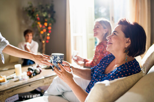 Woman receiving coffee from friend in sunny living room