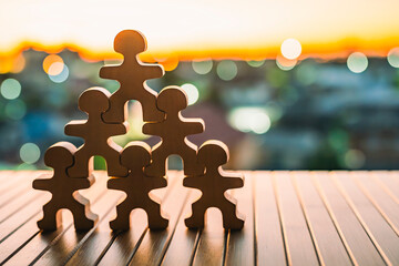 Leadership and teamwork concept with six wooden human figures forming pyramid on table at sunset, symbolizing unity, collaboration, mentoring, organizational strength, and community support.