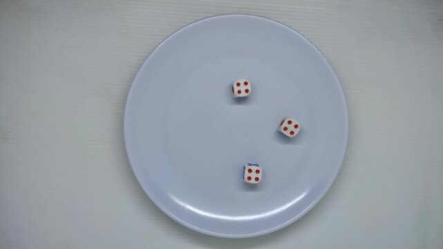 Triple four-value dice. A person reaches into the frame to pick up the dice from the plate, shakes them in their hand, and rolls them onto the white plate until they get three fours.