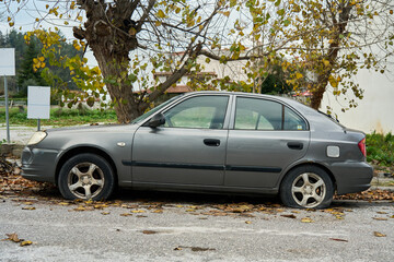Old gray sedan with flat tires parked on a quiet street under autumn trees. Abandoned or neglected car surrounded by fallen leaves, symbol of decay, urban neglect, and seasonal change. © beautiful-photo.de