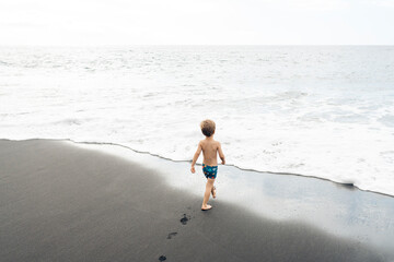 Child running towards ocean on black sand beach