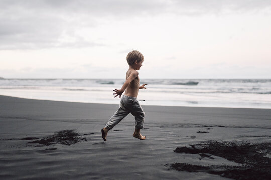Young child running barefoot on black sand beach
