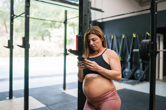 Pregnant woman exercising at gym using smartphone