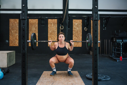 Pregnant woman performing barbell squat in gym