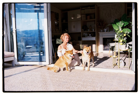 Woman sitting with her two Shiba Inu dogs on the porch of her house 