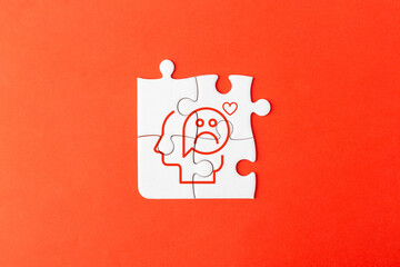 White jigsaw puzzle pieces on a red background forming a human profile with a sad face icon, representing mental health struggles, burnout, emotional stress, depression, and psychological fatigue.