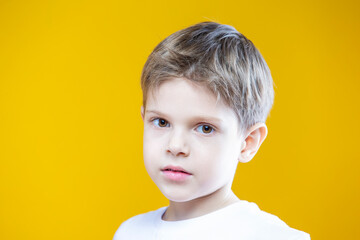 One Adorable Tranquil Little Male Kid Boy Of 5-6 Years Old Wearing White t-shirt Polo Isolated on Plain Yellow Background As Children Indoor Studio Portrait To Convey Childhood Lifestyle Concept
