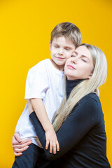 Smiling Cheerful Happy Couple Woman And Child Boy In Casual Clothing Having Mommy Little Kid Son Hug Cuddle While Posing on Yellow To Convey Mother's Love Day
