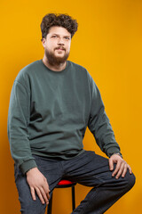 Youth Lifestyle. Caucasian Young Tranquil Brunette Handsome Man in Green Shirt Sweatshirt As Casual Clothes Looking Straight Isolated Over Light Yellow Background Sitting