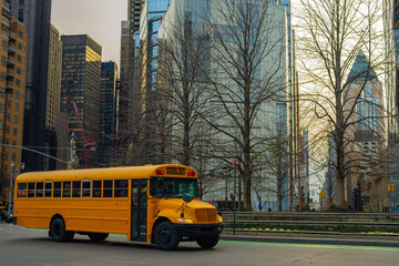 Obraz premium NYC school bus driving through Manhattan street. New York City yellow school bus in urban traffic. NYC transport classic yellow school bus. Manhattan city street with NYC school bus.