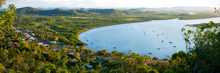 Sunlit river bend backed by mangroves and scattered hillside homes.
