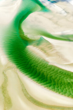 Emerald tidal patterns winding across pale sand flats.