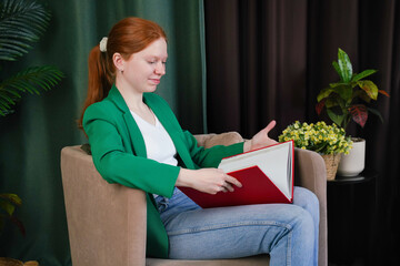 Woman reading a large book while sitting in a cozy chair in a modern indoor setting
