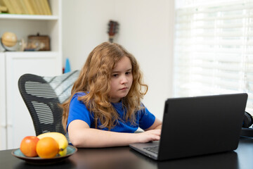 Kid watching educational video on laptop. Boy studying in modern interior. Little student learning online at home. Child typing homework on laptop. Student watching online class.