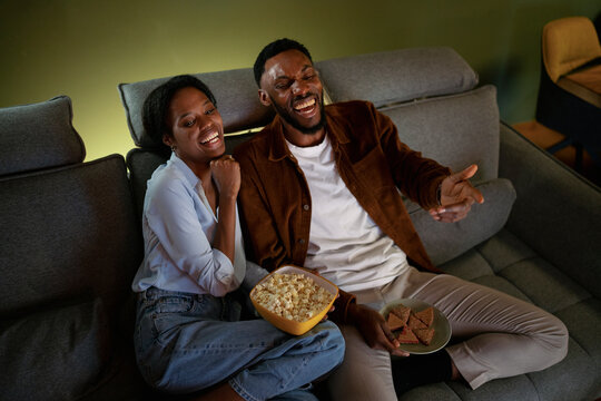 Couple enjoying snacks while laughing on a cozy couch
