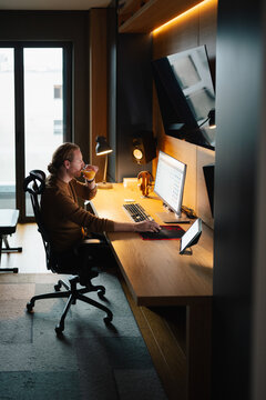 Man working at home office desk while enjoying a warm drink
