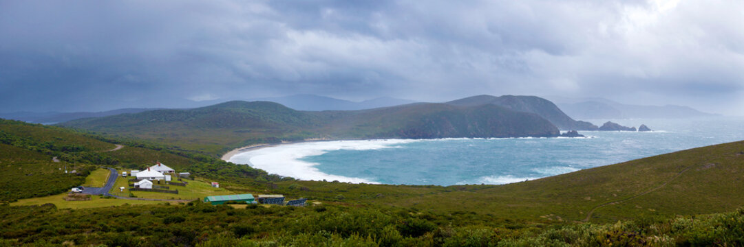 Storm clouds roll in over a secluded bay and rugged coastal hills.
