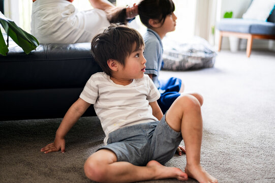 A young boy sits on the carpet with curiosity as family members interact nearby