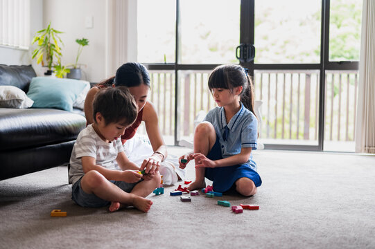 Two children play with colourful building blocks on the living room floor while an adult supervises