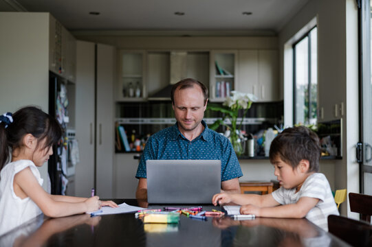 Father with two children seated at a dining table doing art together