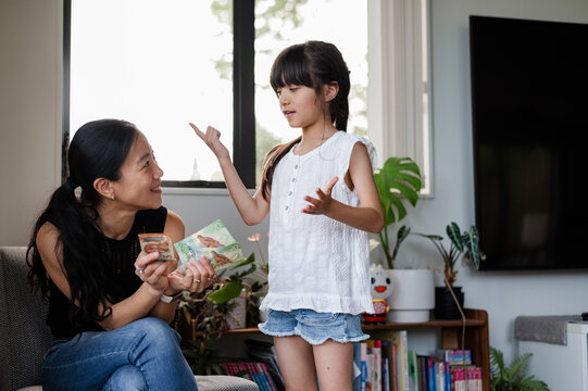 Girl shares excitement about money with her mother in a cosy living room setting