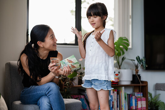 A mother is happily engaging with her daughter while showing her banknotes