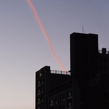 Pink Contrail Touching Silhouetted Buildings at Dusk