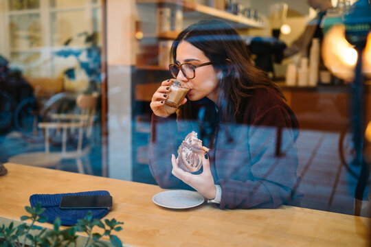 Woman Enjoying Coffee and Pastry at a Caf&eacute; Window