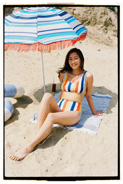 A woman relaxes under a colorful beach umbrella