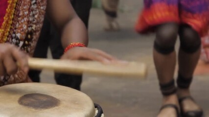 Person playing large brown djembe drum with stick on floor