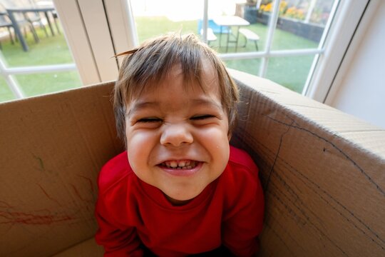 Child with crinkling eyes smiling inside cardboard box