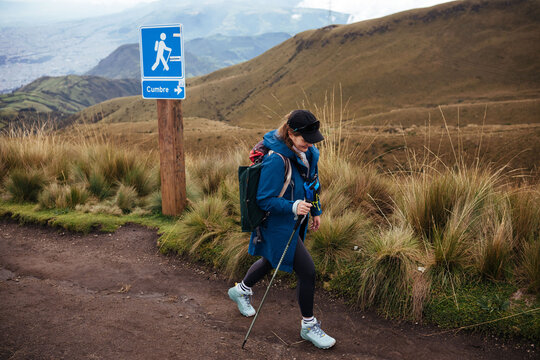 Female hiker walking uphill past summit sign in highland trail