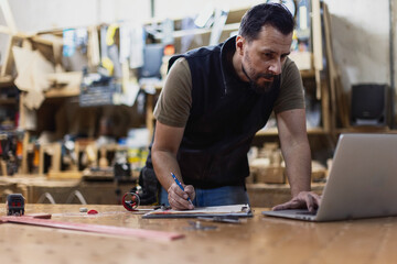 Man works on laptop while taking notes in workshop