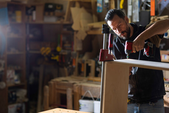 Woodworker assembling furniture in workshop during day