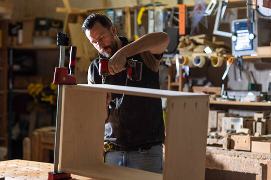 Carpenter Assembling Wooden Cabinet With Cordless Drill