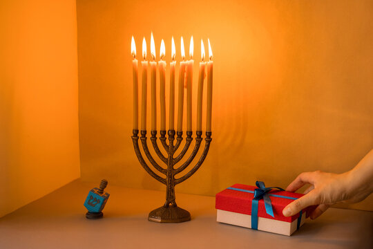 A woman's hand holding a gift box, a dreidel and a menorah.