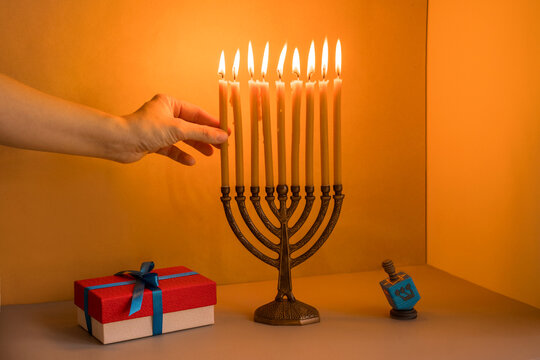 A woman's hand holding a candle in menorah, gift box and dreidel.