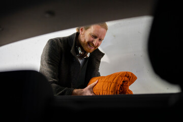 Man takes orange blanket from car indoors during winter
