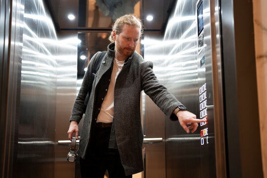 Man presses elevator button while holding camera in modern building
