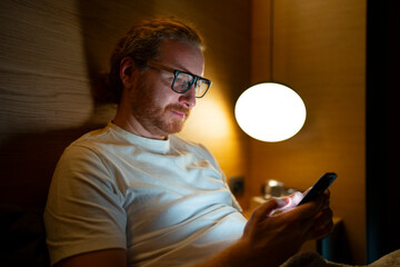 Man using smartphone while sitting in a dimly lit room at night
